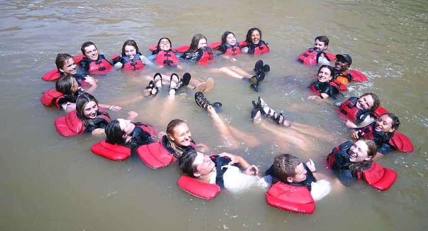 A group of students wearing life jackets float in a circle with their feet floating in the middle of the circle